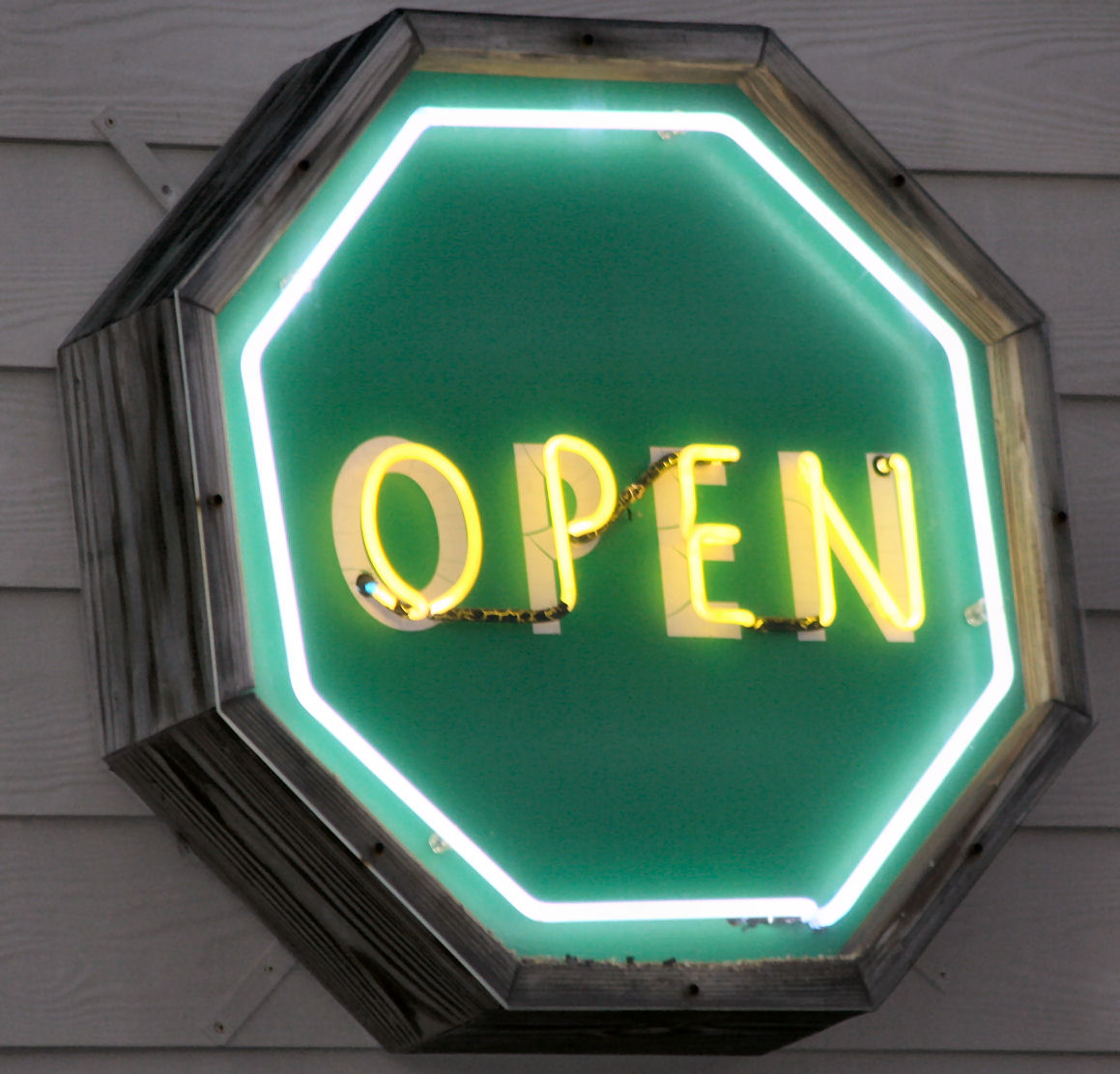 Neon-light sign in the shape of a green octagon with the word open in the middle in yellow neon light.