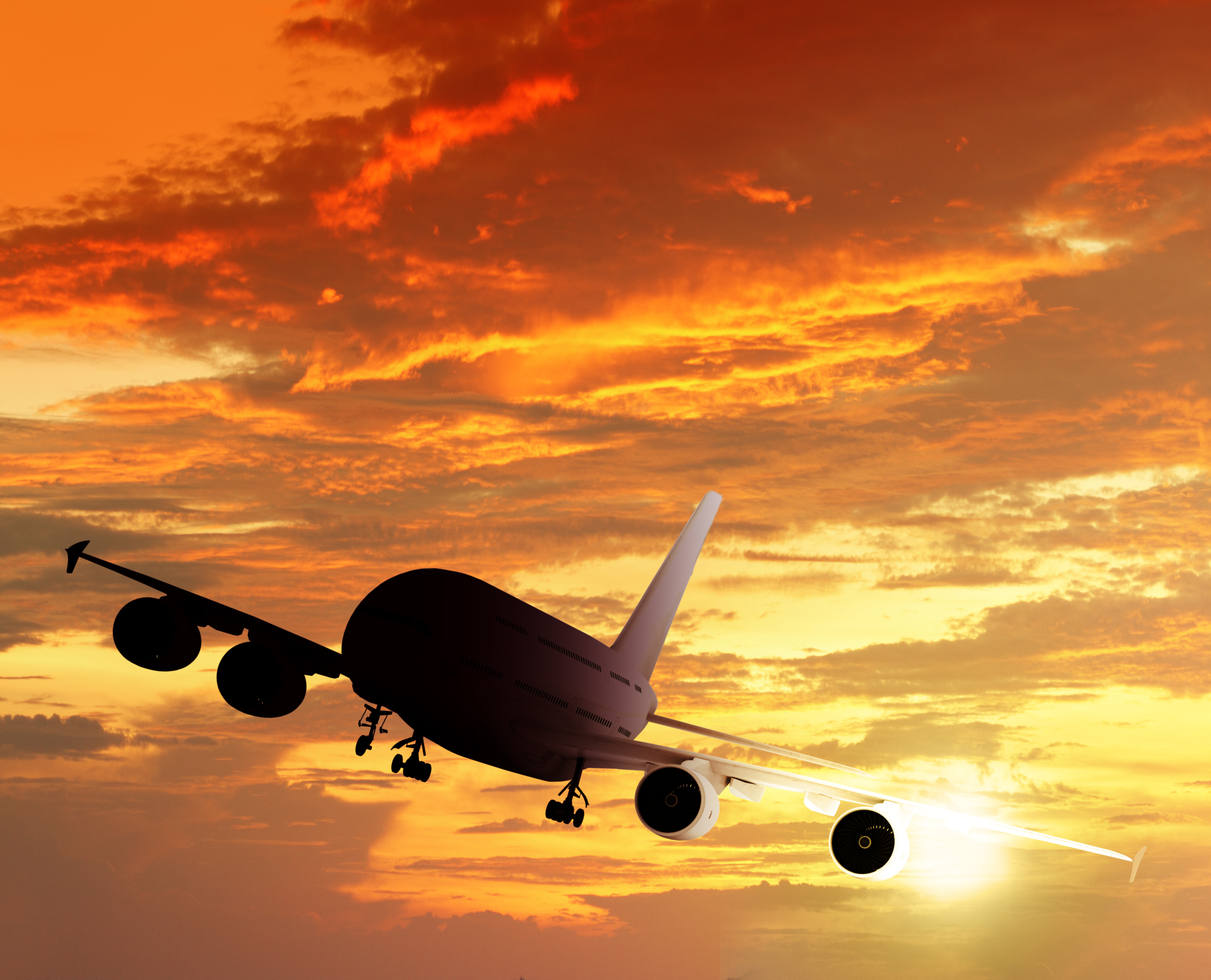 Silhouette of plane in the air with a sunset in the background.