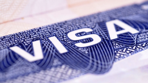 A close‑up of a visa document with bold white letters on a blue patterned background. A passport is slightly visible underneath.