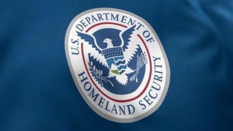 A blue flag shows the seal of the U.S. Department of Homeland Security. The round emblem has an eagle and detailed symbols.