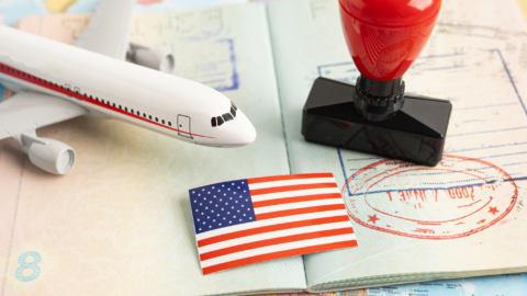 A few travel items, including a plane model and a US flag, rest on an open passport. The setup gives a simple hint of a journey ahead.