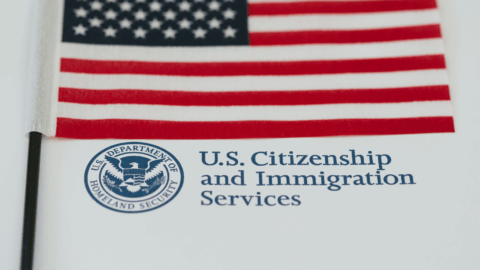 An American flag sits on top of a page featuring the U.S. Citizenship and Immigration Services name and seal. The scene highlights themes of immigration, citizenship, and national pride.