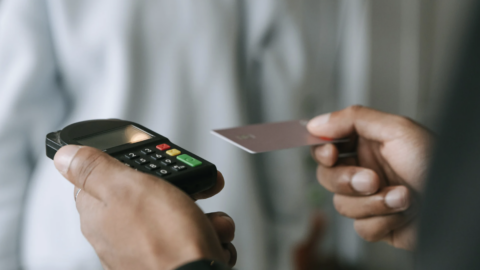 A person is holding out a card to pay. Another person is holding the machine to take the payment.