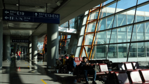 A group of people sit on benches in an airport terminal. Travelers wait in a modern airport space.