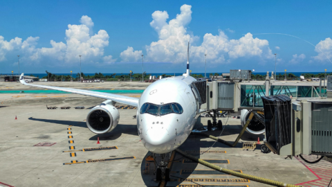 A plane is parked at the gate on a sunny day. The sky is clear with big fluffy clouds.