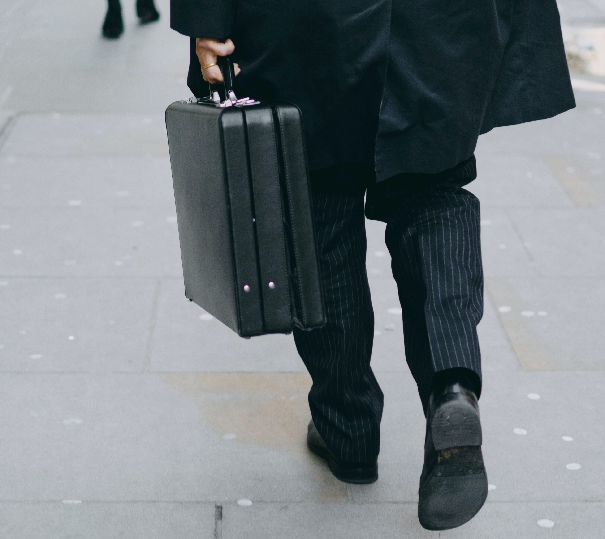 A man's bottom half walking in business clothes with a briefcase in hand. The photograph is from behind the subject.