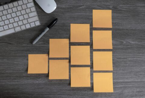 Multiple orange post-it notes making a pyramid shape laid flat on a table with a laptop.