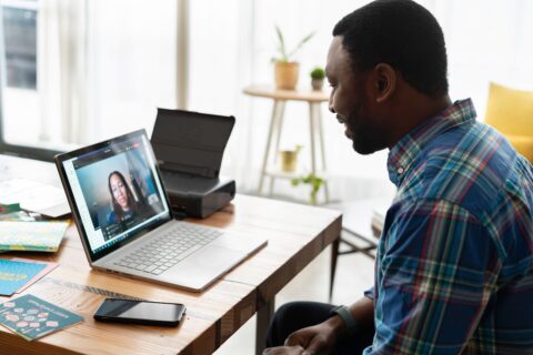 A man is sitting at his laptop on a video call with a woman on the laptop screen.