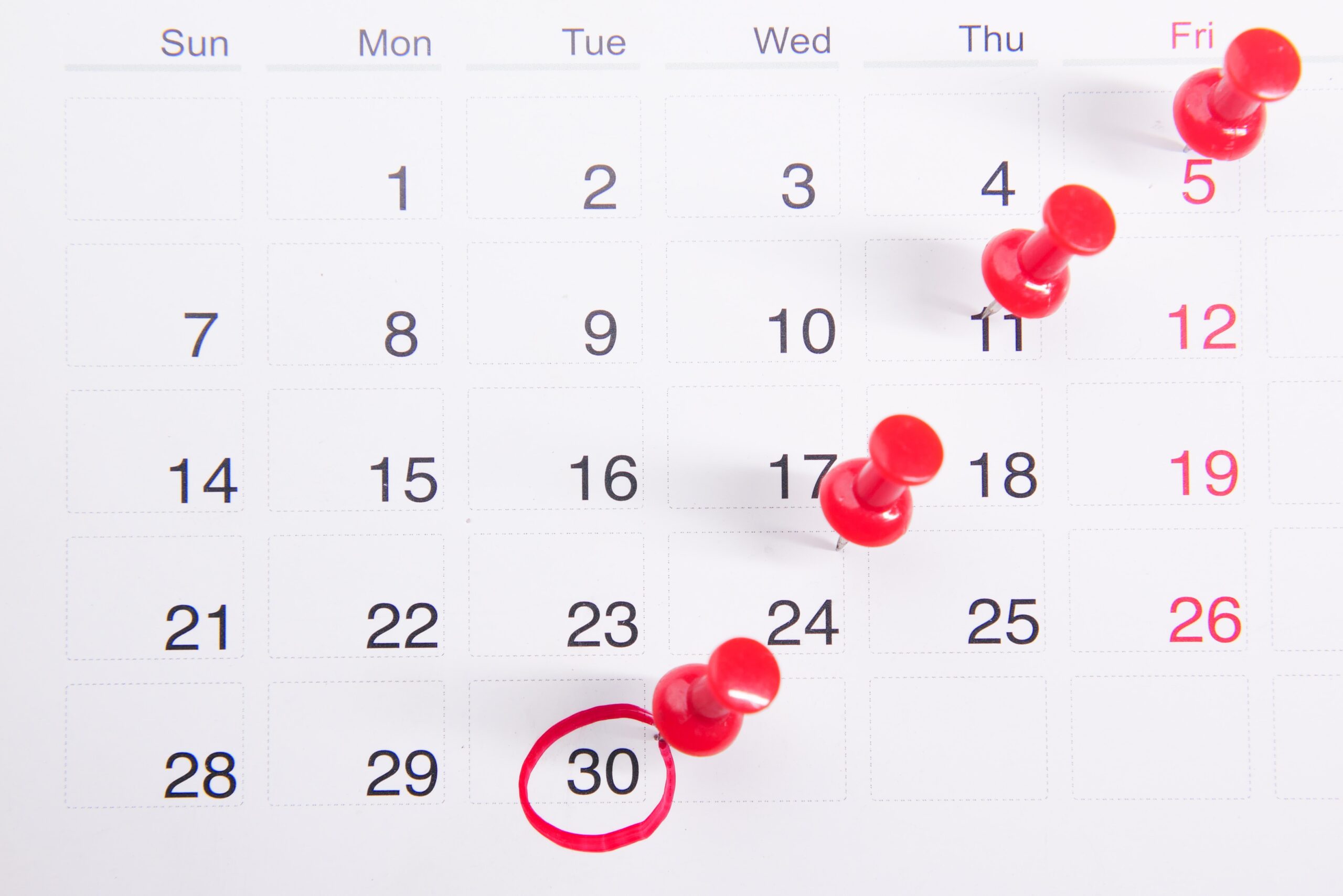 White calendar with red push pins on dates and the end of the month is circled in red ink.